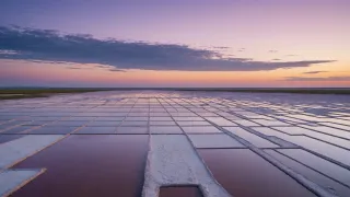 Bassins d'évaporation d'eau de mer au crépuscule, croûtes de sel blanc sur les bordures et ciel rose et violet reflété dans l'eau