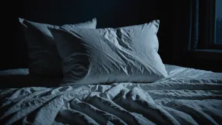 Oreillers et draps froissés d'un lit vide, éclairés par la seule lueur bleutée de la lune dans une chambre obscure